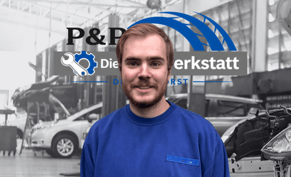 Kfz-Mechatroniker in blauer Kleidung in der Autowerkstatt Delmenhorst vor Werkstattlogo